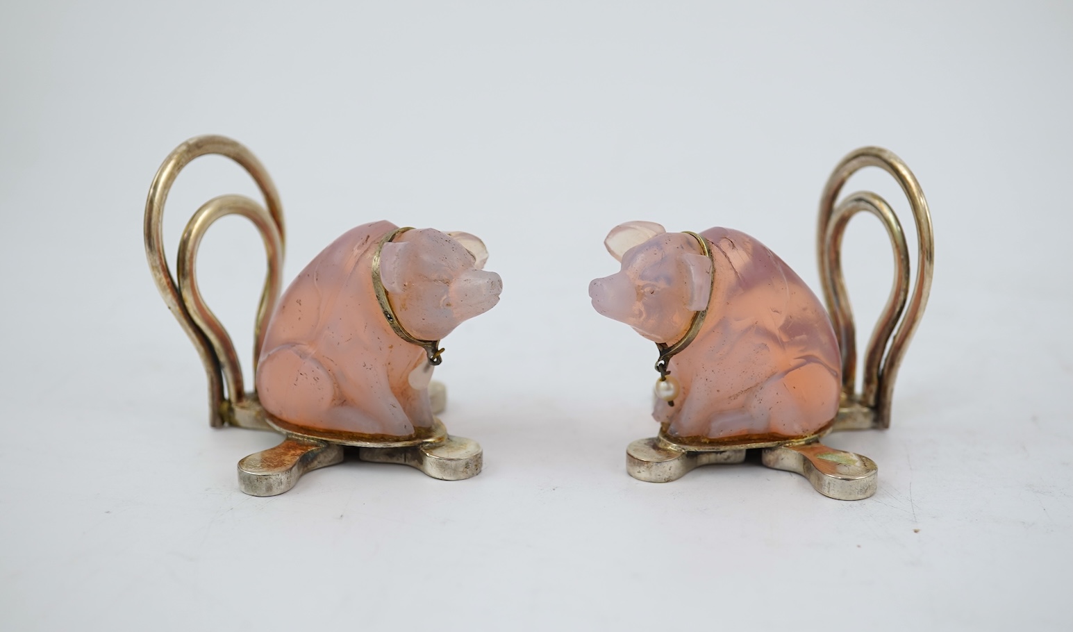 A cased pair of unusual Edwardian silver and pink glass mounted menu holders, by William Comyns, each modelled as a seated pig with collar